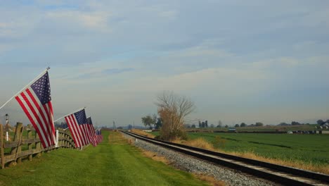 una vista de una sola vía ferroviaria, con una valla con la bandera de américa en ella, agitando suavemente en el viento en un soleado día de otoño