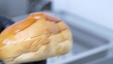 close-up of a hamburger bun being sliced in half by hands wearing black latex gloves for food safety in a restaurant