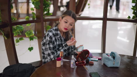 una joven bonita aplicando polvo a su cara usando un pincel, artículos cosméticos como fundación, lápiz labial y un compacto están esparcidos en la mesa, con un fondo borroso