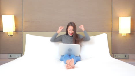 una mujer sentada descalza en la cama usando una laptop aplaude cuando gana un juego