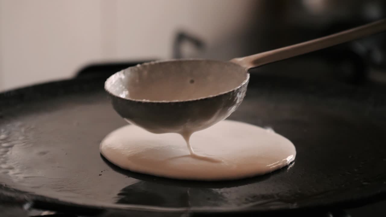 un primer plano de hacer 'dosa' caliente y humeante en una sartén de hierro fundido.