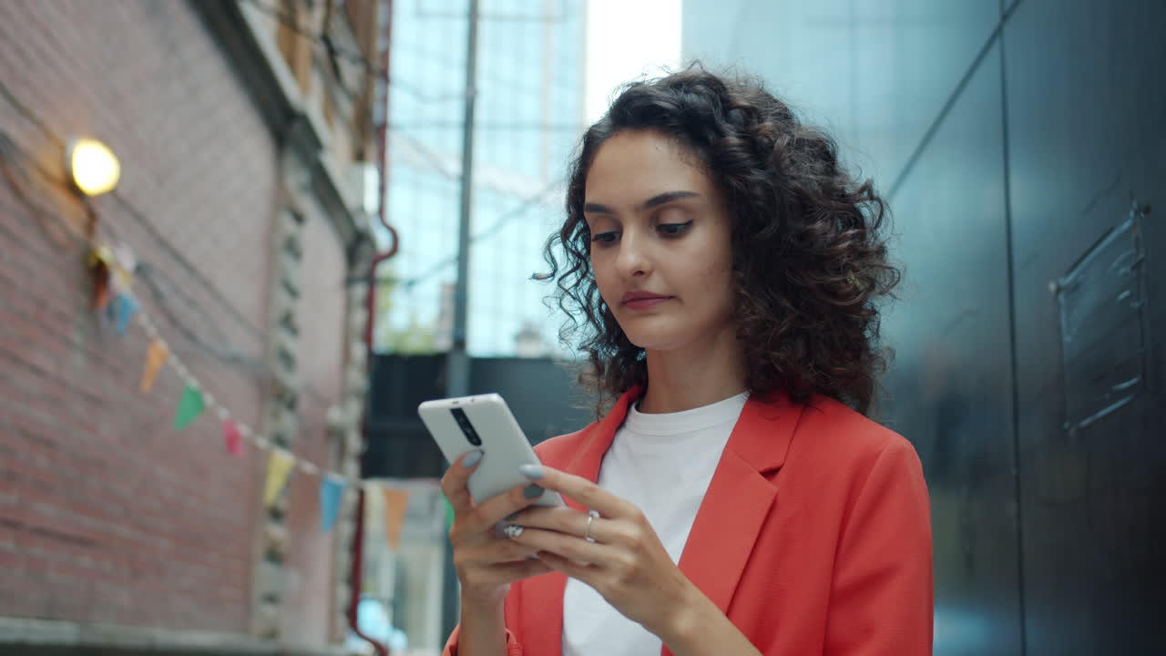 Giovane donna che scrive messaggi sullo smartphone in un vicolo di città