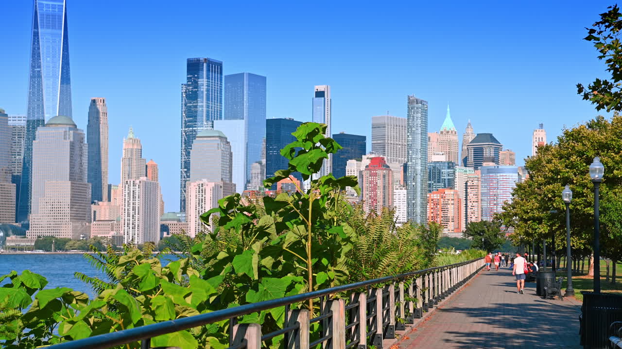 Jersey City, EUA, 1 de julho de 2025: passarela no parque de Jersey City com plano de fundo da silhueta de Manhattan. Pessoas passeiam por uma passarela verde no parque de Jersey City com os arranha-céus de Manhattan ao fundo.