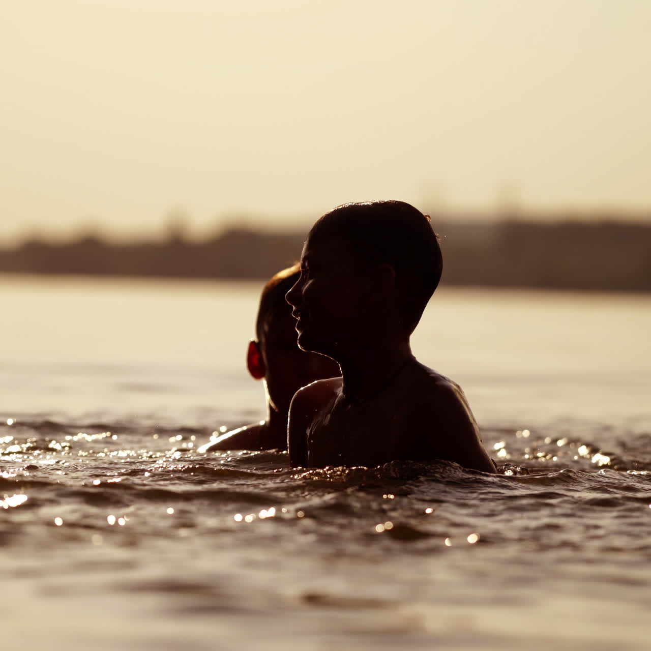 Silhouette of two boys swimming and playing with water at sunset. Happy brothers having good time together in the river in the evening. Close-up.