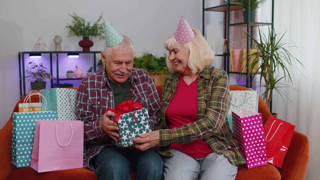 Anziani nonni felici, uomo e donna, che festeggiano un compleanno o un anniversario sul divano di casa