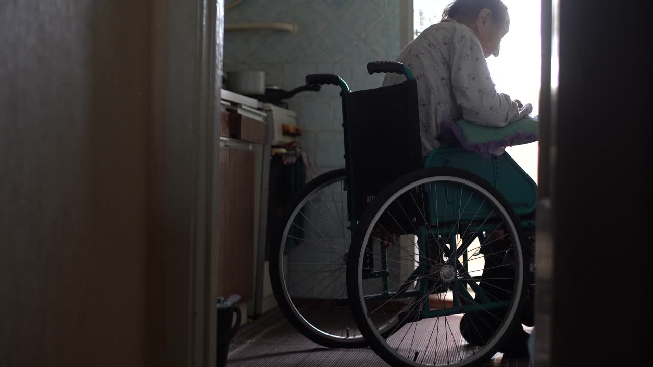 anciana solitaria sentada en una silla de ruedas cerca de la ventana en su casa