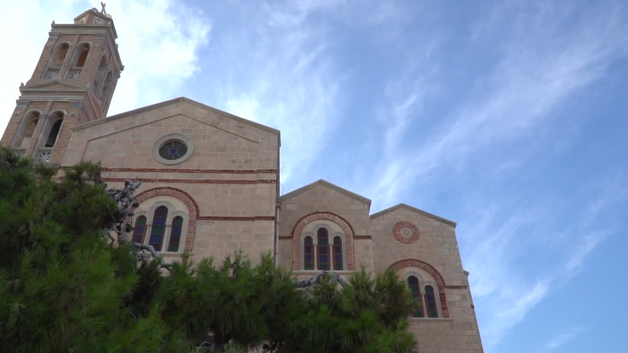 오른쪽에서 왼쪽으로 느린 팬은 전경에 나무가 있는 푸른 흐린 하늘을 배경으로 아름다운 교회를 올려다봅니다.