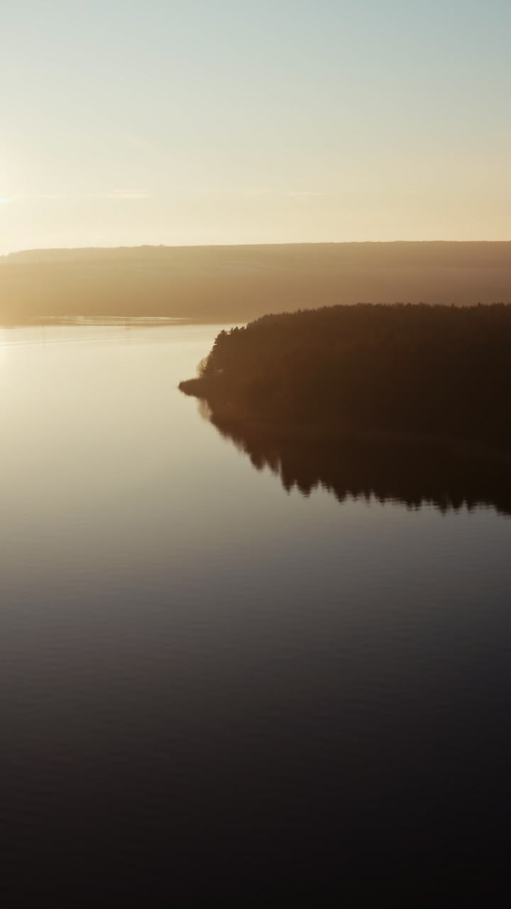 Beautiful view of a sunset on a river. Cinematic footage on the evening river. Sun setting in nature. Aerial view. Vertical video