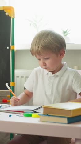 diligent little boy does difficult homework sitting near blackboard with maths problems. student wipes forehead and touches chin solving tasks in class