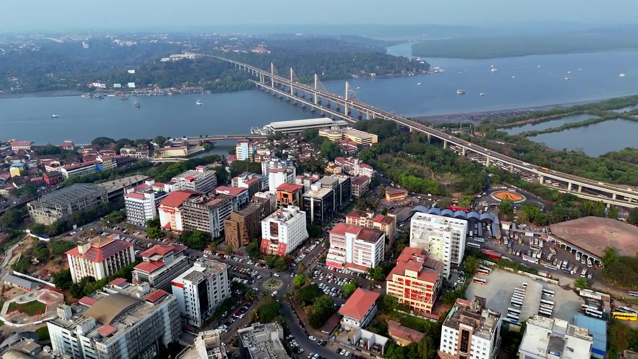 Veduta aerea cinematografica dell'intera città di Panaji che mostra un vivace paesaggio urbano con edifici fitti, strade trafficate e il fiume Mandovi che scorre accanto, con l'Atal Setu che si estende all'orizzonte