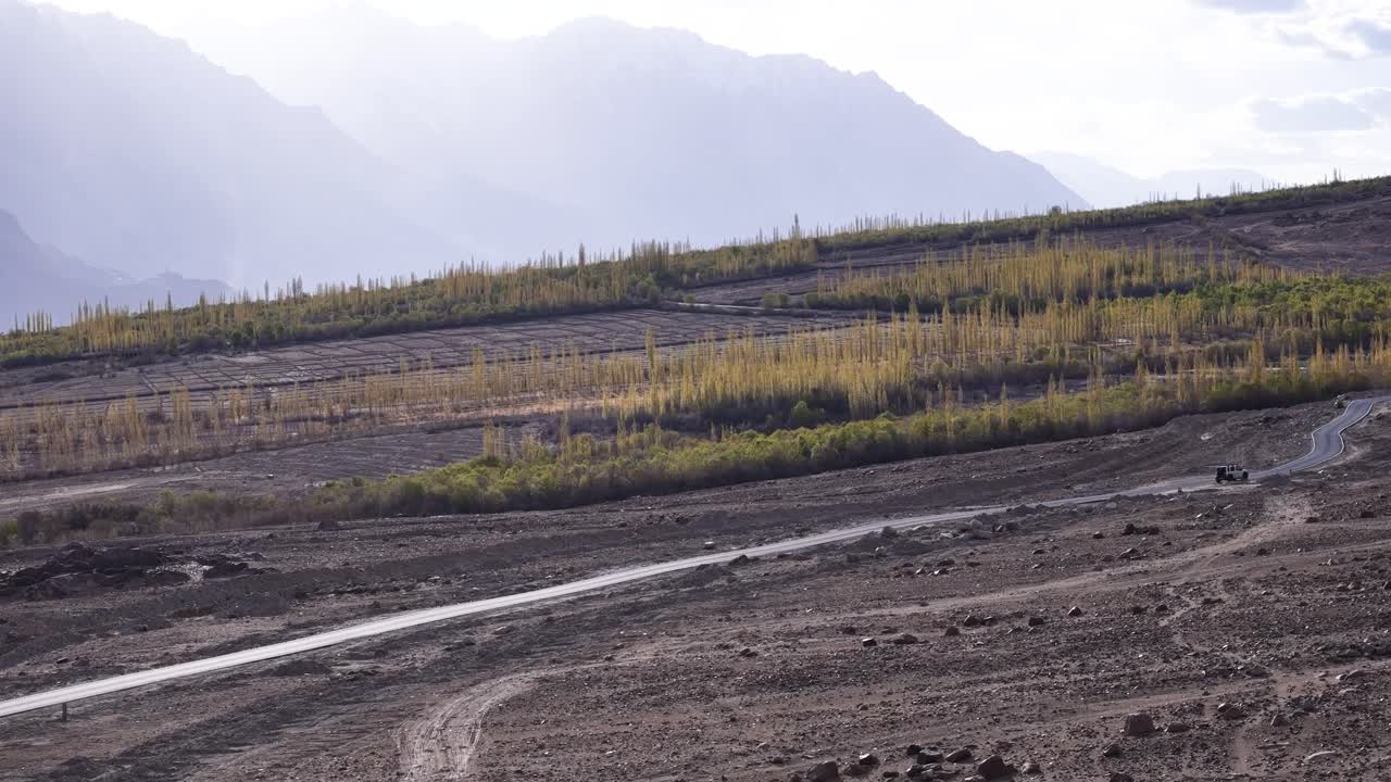 Aerial drone shot following a car driving along the winding mountain roads of Ladakh, surrounded by rugged terrain.
