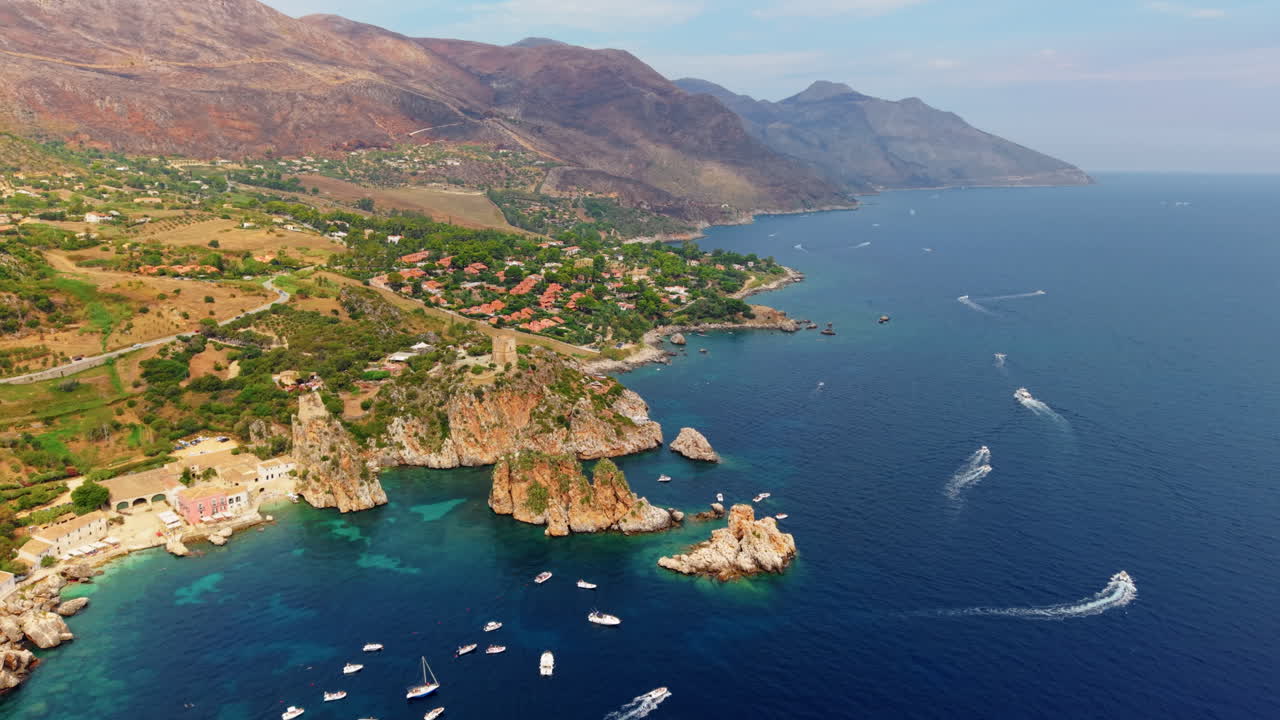 Drone pulling back above Scopello marina with rocky coast, boats, and mountain backdrop