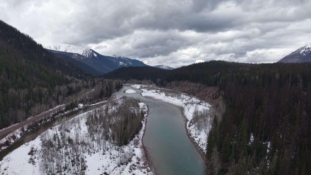 Ripresa aerea con drone di un fiume tortuoso che serpeggia attraverso una valle innevata con foreste sempreverdi e montagne aspre vicino a Whitefish, Montana