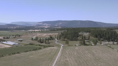 Vuelo-Aéreo-Sobre-Tierras-Agrícolas-Industriales-Montañas-Desnudas-Dentro-De-Un-Valle-Con-Carreteras-Con-Curvas-Pinos-Altos,-Graneros-De-Ganado-De-Trigo-Lechero-En-El-Campo-En-Columbia-Británica-Junto-A-La-Autopista-A-Alberta-Ca-1-5