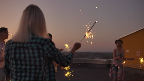 The-company-of-young-people-moves-their-hands-and-body-on-the-roof-with-big-bengal-light-before-night.-They-celebrate-the-birth-of-a-friend.