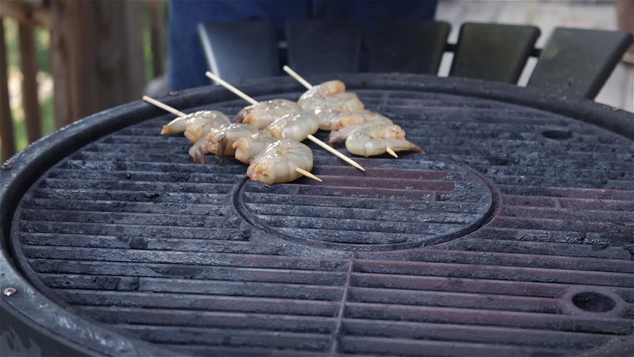 Close up of a hand setting shrimp kabobs on skewers on a hot grill