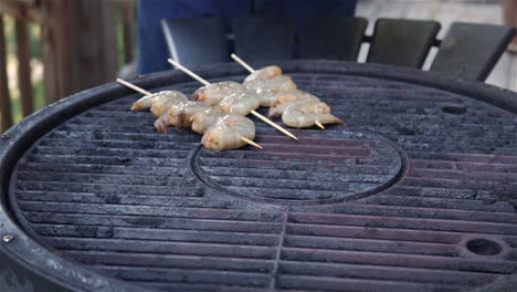 close up of a hand setting shrimp kabobs on skewers on a hot grill