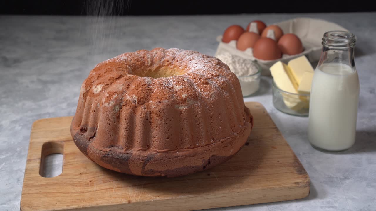 Powdered icing sugar falling on to appetising bundt cake, fresh homemade tasty marble cake.
