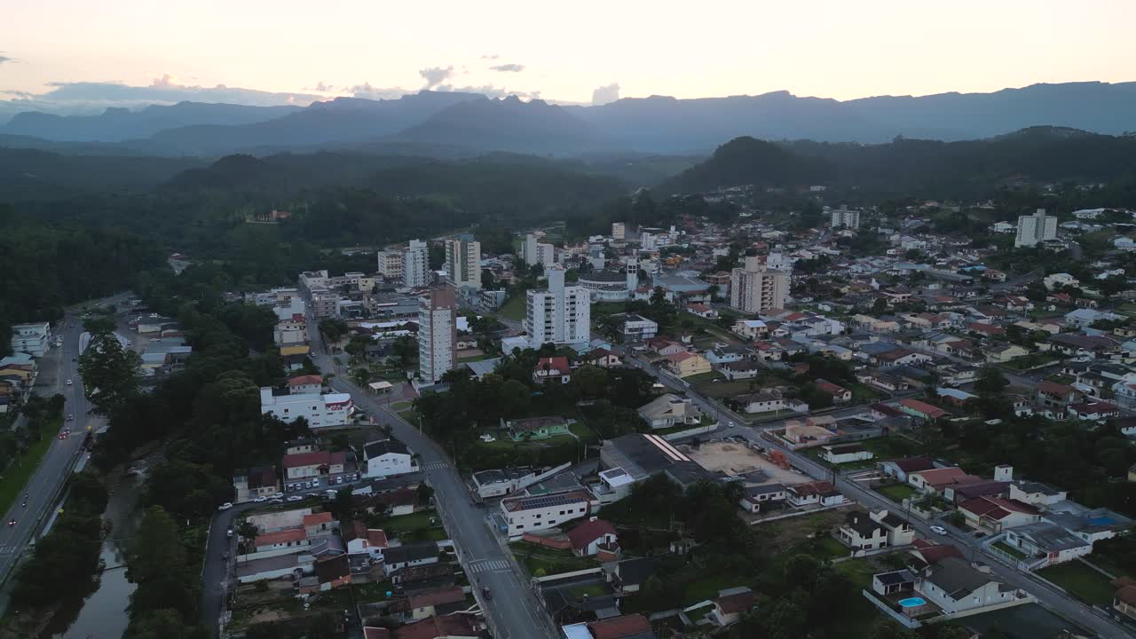 Ampia veduta aerea di Lauro Muller, Santa Catarina, Brasile, durante la luce soffusa dell'alba o del tramonto. Moderni grattacieli si ergono sopra le case basse, circondati da spettacolari montagne verdi.