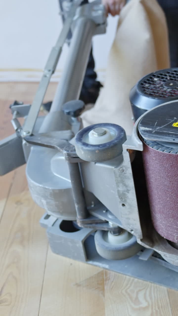 Worker leans floor sanding machine on side and replaces sander belt, vertical