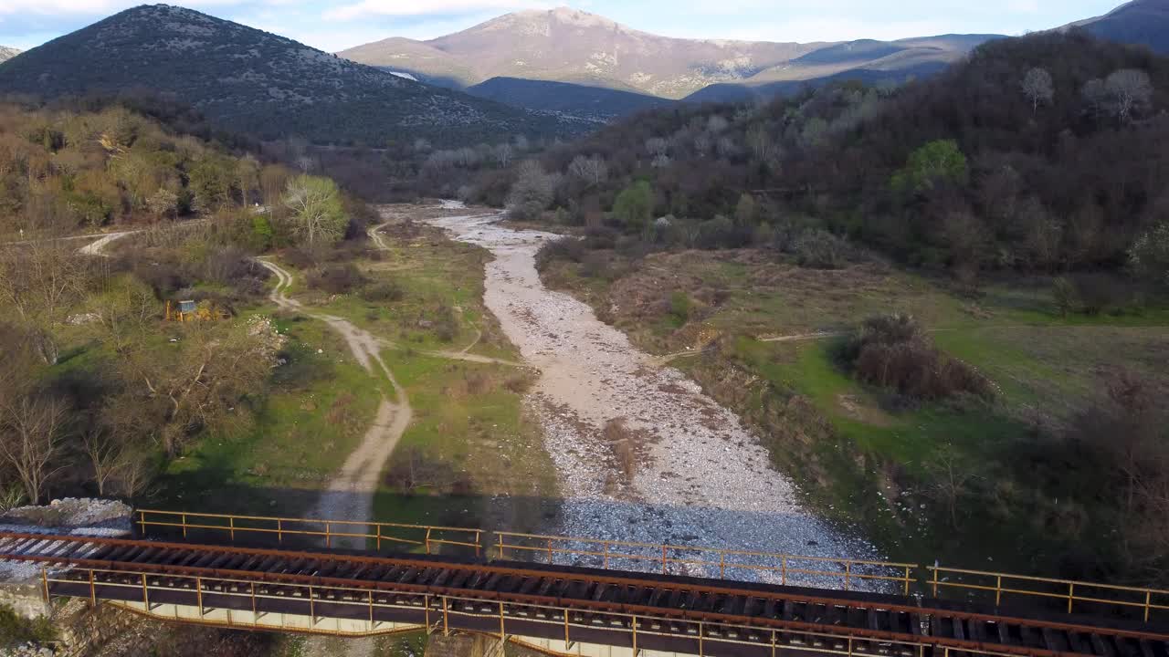 ascender por el aire sobre vías de tren abandonadas en el lecho de un río secado rodeado de montañas