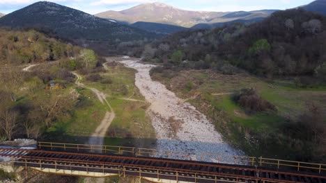 aerial ascend over abandoned train tracks on dried-up riverbed surrounded by mountains