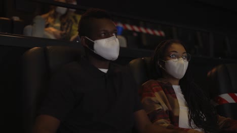 African-American-couple-enjoying-film-during-pandemic,-wearing-white-face-masks