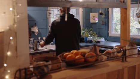 warm kitchen scene with blue walls, rustic wooden table, and a man entering, symbolizing home comfort and family togetherness. natural light and fresh fruits enhance the ambiance.