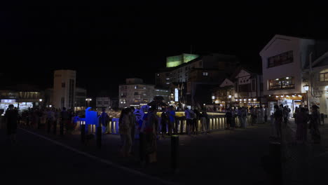 Masked-tourists-walking-around-and-taking-pictures-of-the-famous-Kusatsu-Yubatake-in-a-cool-summer-evening-after-the-light-up