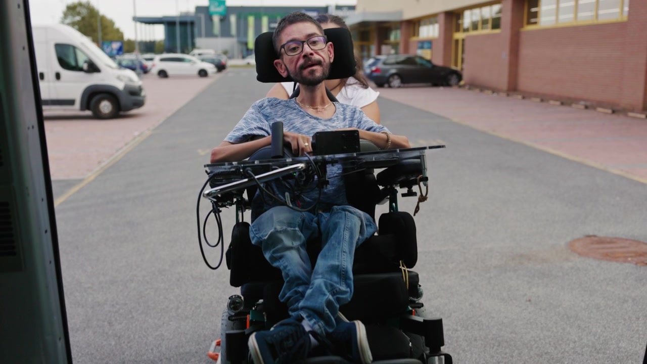 Powered wheelchair user boarding an adapted vehicle with support from an assistant and an accessible