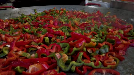 Red-and-Green-sliced-peppers-on-huge-street-vendor-frying-pan,-Closeup-Push-In