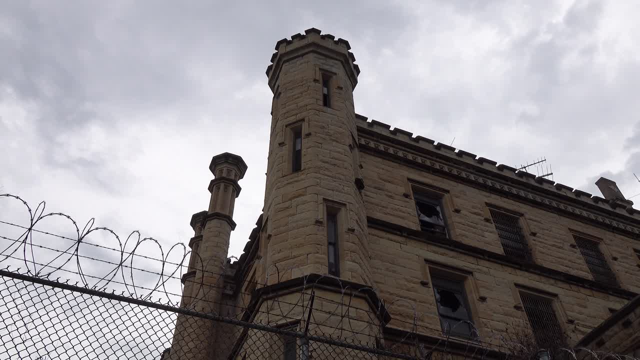 Timelapse of old historic state prison jail with gloomy dark  clouds passing over gothic brick prison cell house and barbed wire fence