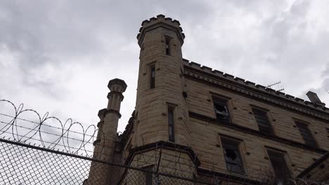 timelapse of old historic state prison jail with gloomy dark  clouds passing over gothic brick prison cell house and barbed wire fence