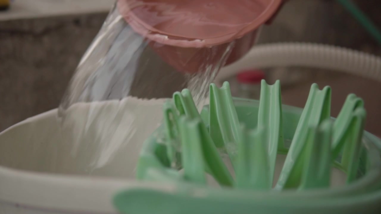 Primo piano di acqua versata in un contenitore domestico usando un mestolo di plastica durante la routine di pulizia in ambiente domestico