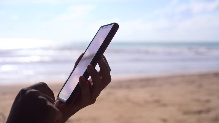 Mano di donna che usa lo smartphone con sfondo di spiaggia.