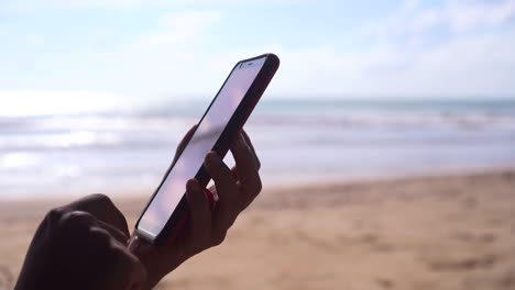 la mano de una mujer usando un teléfono inteligente en el fondo de la playa.