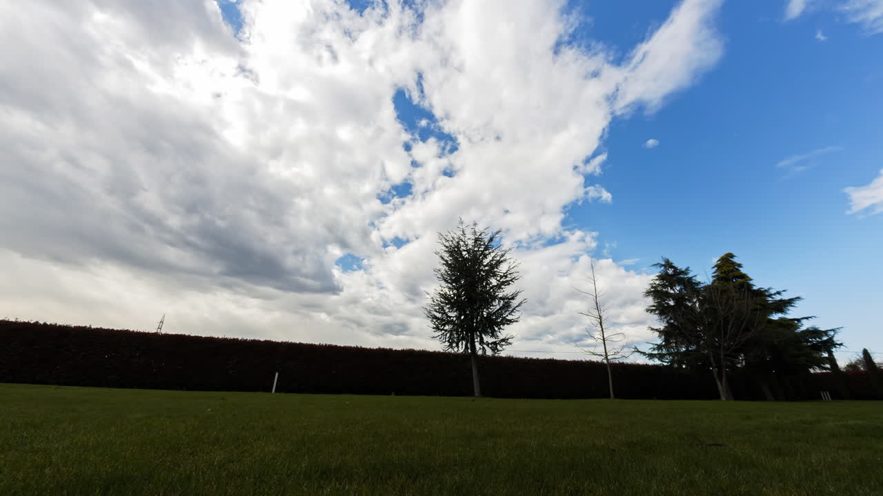 화창한 날 푸른 하늘에 흰 구름이 장관을 이루며 울타리와 나무가 있는 푸른 잔디의 전망 - 타임랩스 와이드 샷