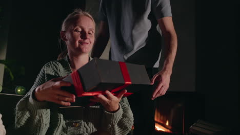 couple opening a christmas gift by the fireplace