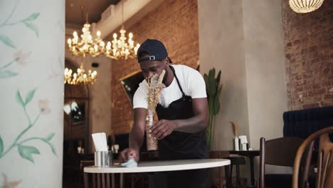 a black person in a black apron and white t-shirt wipes the table with a special towel in a cafe. high quality video