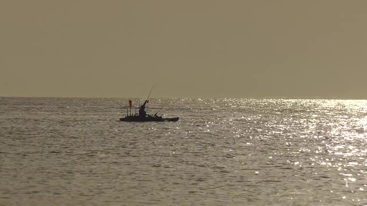 Silhuett av kvinne som fisker fra kajakk på rolig solbelyst hav ved daggry