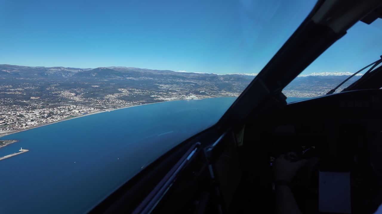 Tampilan dari kokpit pilot saat tiba di bandara Nice, bermanuver di atas Laut Mediterania di sebelah French Riviera, dengan Pegunungan Alpen yang tertutup salju di belakang. Tampilan kokpit imersif