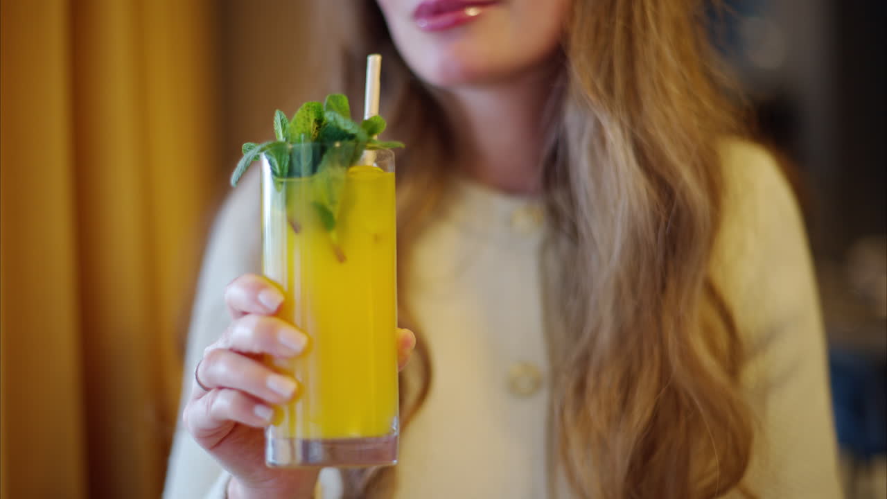 Woman drinking fresh orange lemonade with mint leaves and paper straw