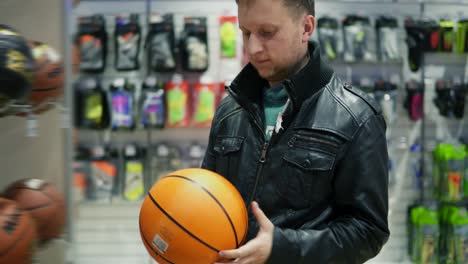 an adult man in black leather jacket choosing a basketball ball in a sports store