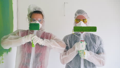 couple in workwear with respirators holds rollers in room