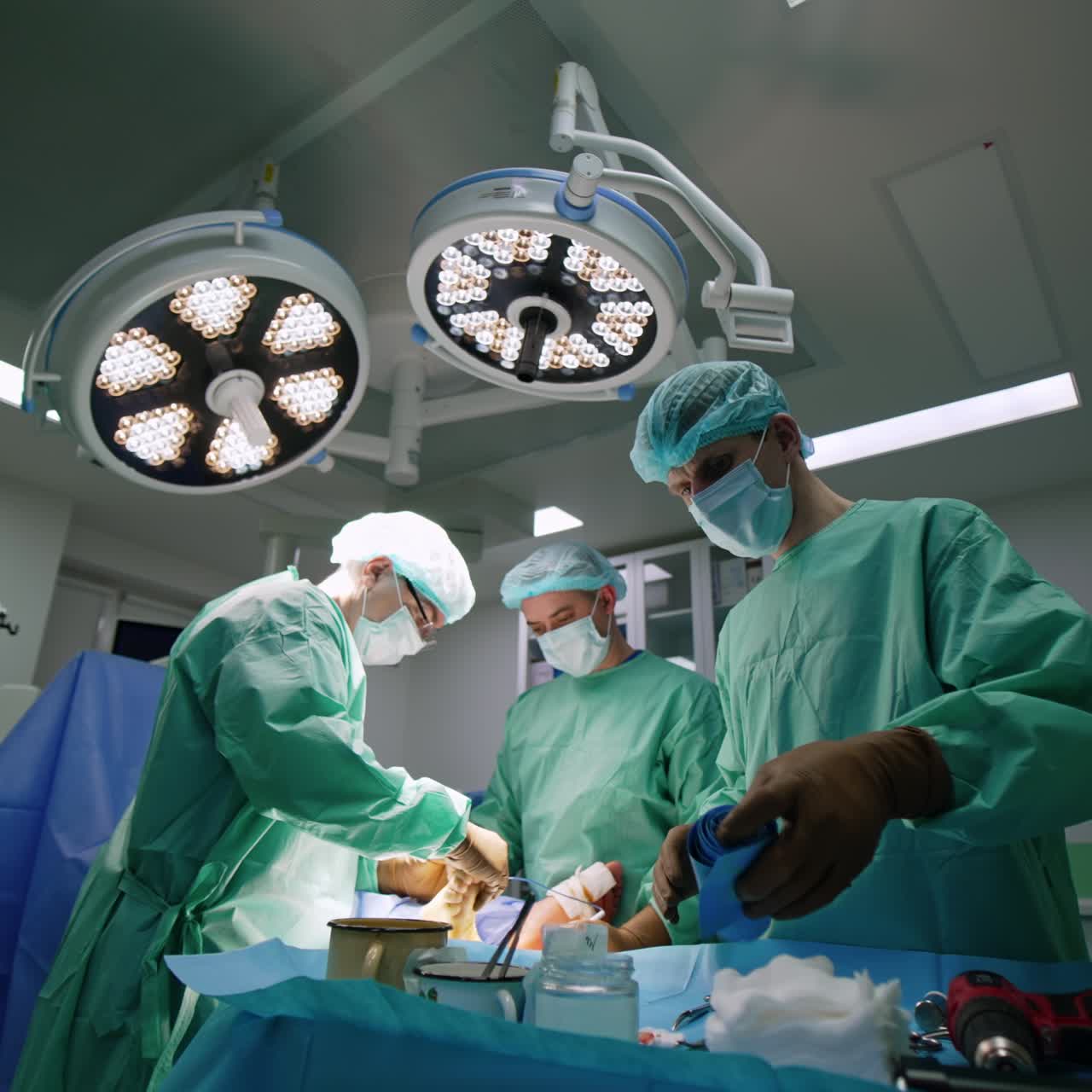 Male assistant at surgery rolls the bandage. Two surgeons operate the foot of patient