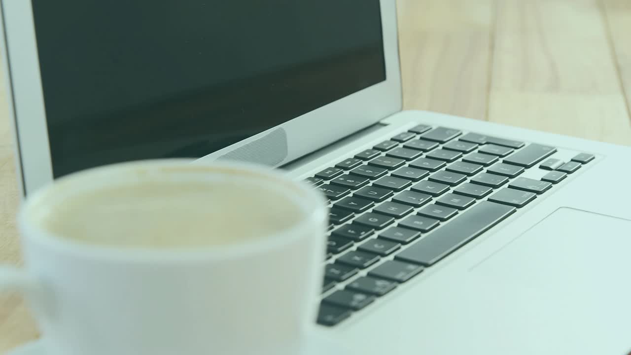 Blue particles drifting around coffee cup beside laptop, forming shield padlock lines for security