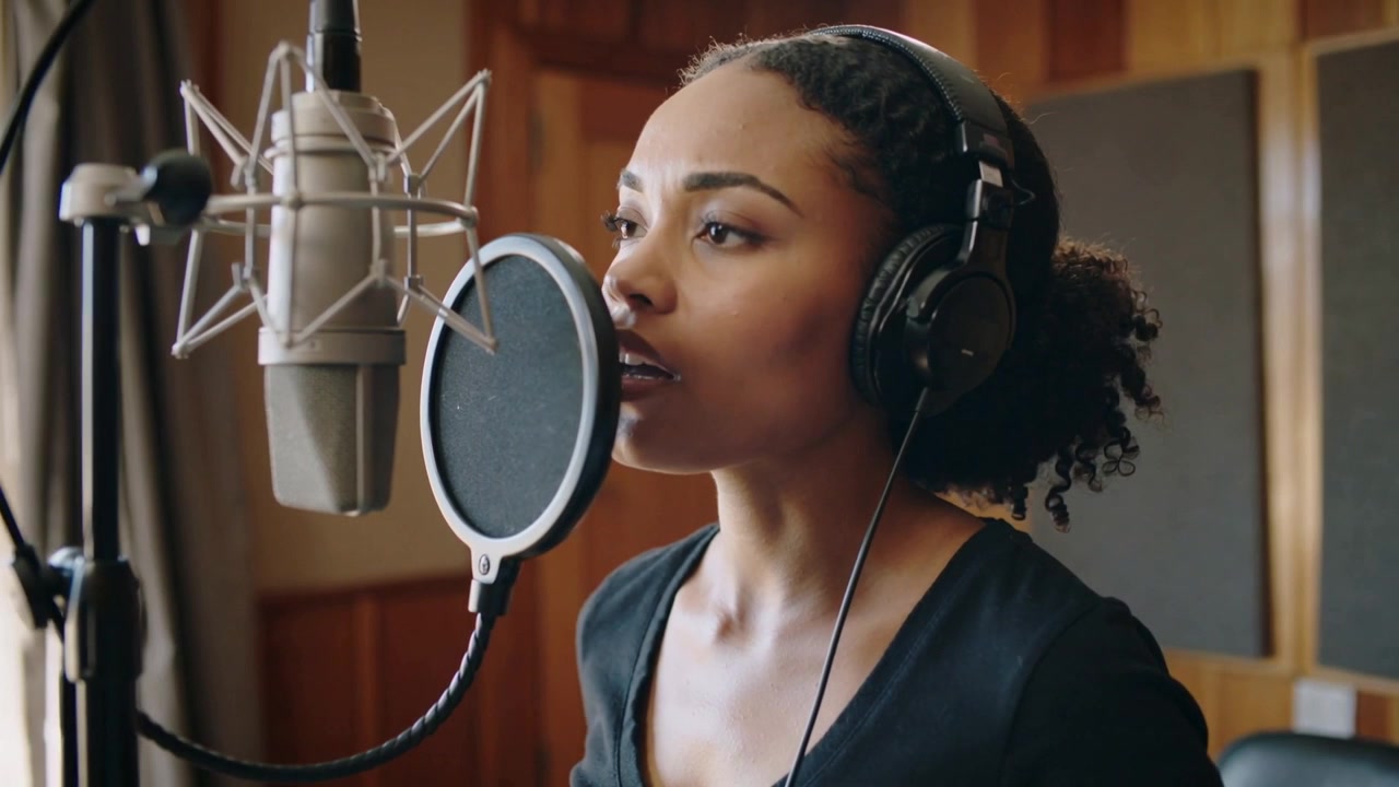 Inizio ripresa, cantante con cuffie che canta, plasma le frasi in studio con microfono, filtro anti-pop e pannelli acustici.