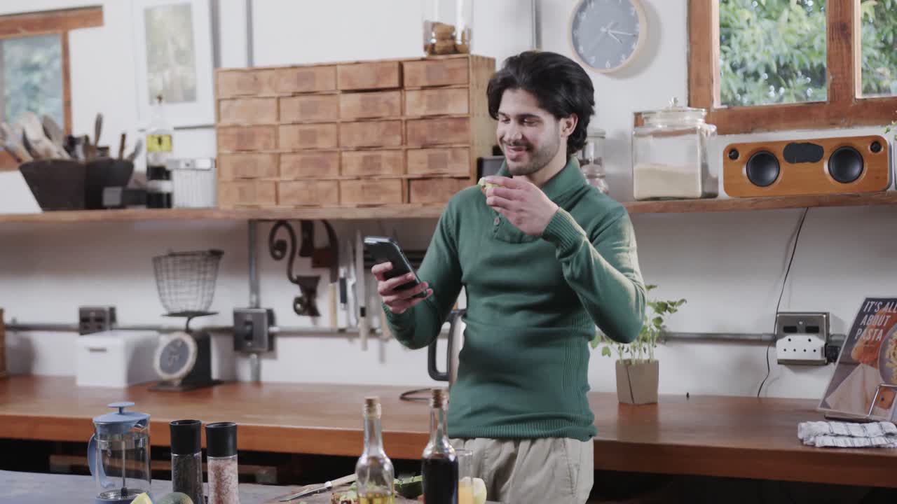 Uomo caucasico che mangia toast all'avocado e usa lo smartphone in cucina, al rallentatore