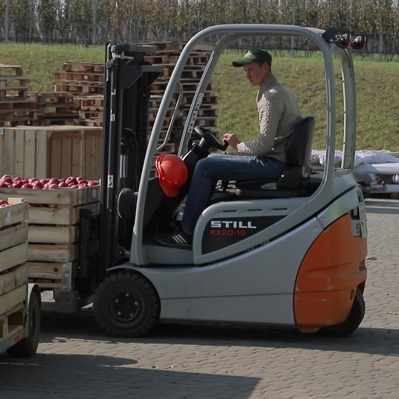 A man on a new forklift truck pulls up quickly to the pallet with red apples, lifts it and takes it to a warehouse. Close-up.
