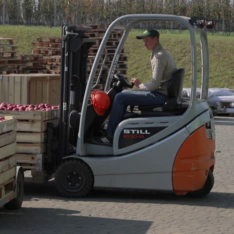a man on a new forklift truck pulls up quickly to the pallet with red apples, lifts it and takes it to a warehouse. close-up.